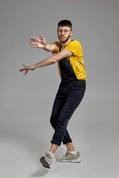 Full-length portrait of a funny guy dancing in studio on a gray background. - Photo, Image