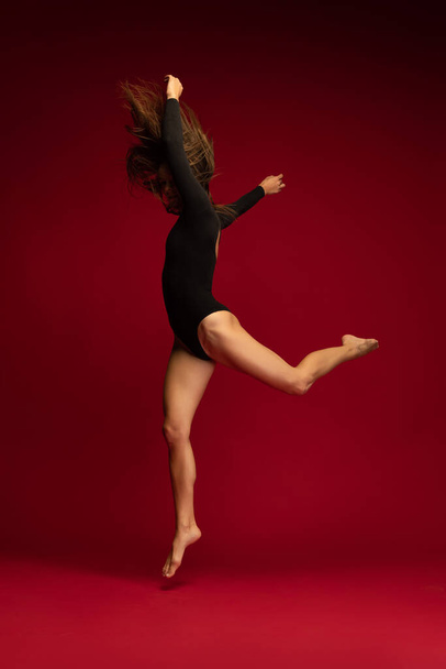 Dynamic portrait of young flexible contemp dancer dancing isolated on dark red background. Art, beauty, inspiration concept. - Fotografie, Obrázek
