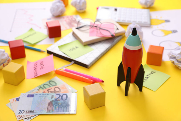 Composition with toy rocket, stationery and money on yellow background. Startup concept - Foto, afbeelding