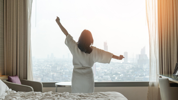 Hotel pihenés lusta napon ázsiai nő felébred a jó alvás az ágyon hétvégén reggel pihenés a kényelmes hálószoba felé néző városi kilátás, amelynek boldog, munka-magánélet minőségi egyensúly életmód - Fotó, kép