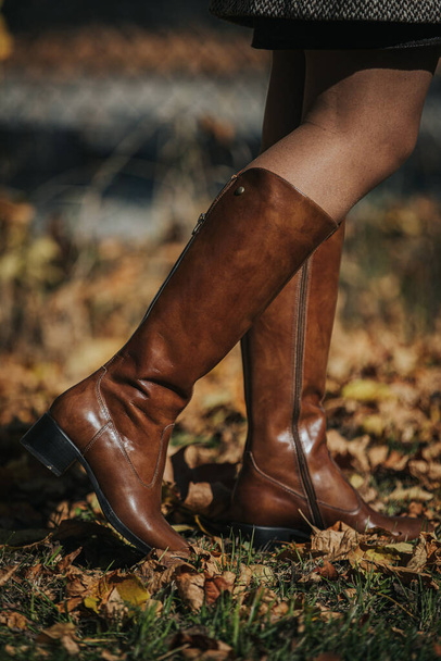 A woman wearing a brown fashionable boots while walking on autumnal leaves - Photo, image