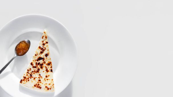 Egy szelet hagyományos finn nyikorgó sajt felhőbogyós lekvárral a tányéron fehér alapon. - Fotó, kép