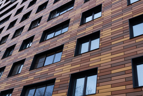 Wand eines modernen, trendigen Gebäudes mit Fenstern mit einer abstrakten, braunen, rechteckigen Fassade aus Fliesen. Stadtlandschaft. Nahaufnahme - Foto, Bild