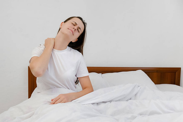 Fibromyalgia and backache concept. Unhappy young girl waking up in uncomfortable bed feeling ache in back pain massaging tensed muscles of stiff neck after sleep on bad mattress in incorrect posture - Фото, зображення