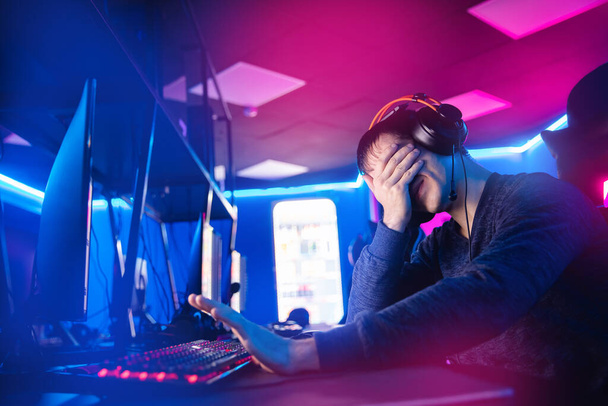 Streamer young man facepalm professional gamer playing online games computer with headphones, neon color - Foto, imagen