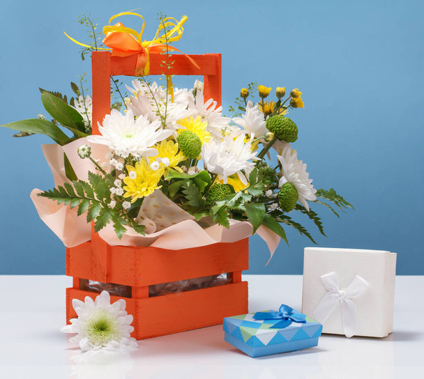 Beautiful bouquet of various flowers and gift boxes on the blue background. - Fotó, kép