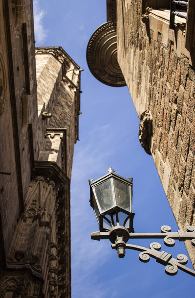 A low angle of a metal lamp between buildings of church and a blue sky - Fotografie, Obrázek