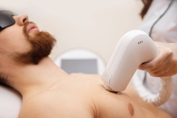Koncept laserové depilace pro muže. Kosmetický salon pracovník aplikuje léčbu chlap odstranění ochlupení - Fotografie, Obrázek
