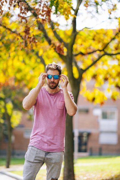 A young Caucasian stylish man wearing a nice pink t-shirt and sunglasses walking on a street - Foto, afbeelding