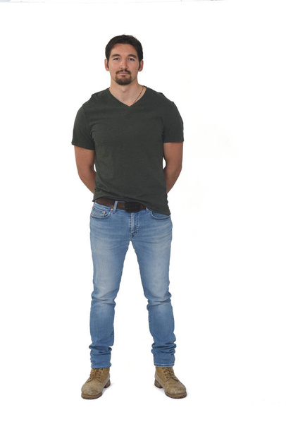 retrato completo de un hombre con jeans, mano sobre espalda mirando a la cámara sobre fondo blanco - Foto, imagen