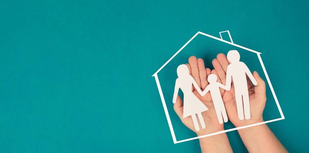 A family, mother, father and child in silhouette, paper cut out, holding in hands, roof of a house, petrol colored background - Foto, imagen