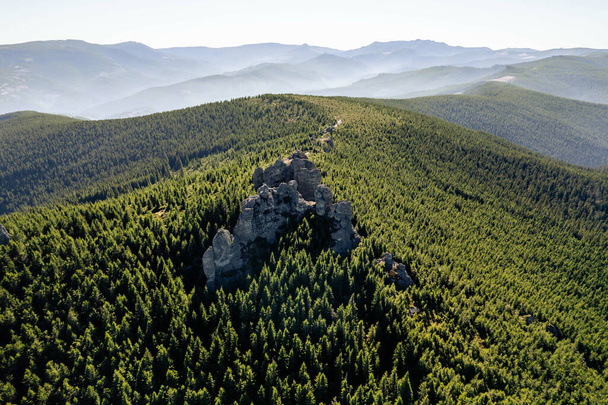 An aerial shot of a big rocks on a big mountain covered with green in a sunny day - Photo, Image