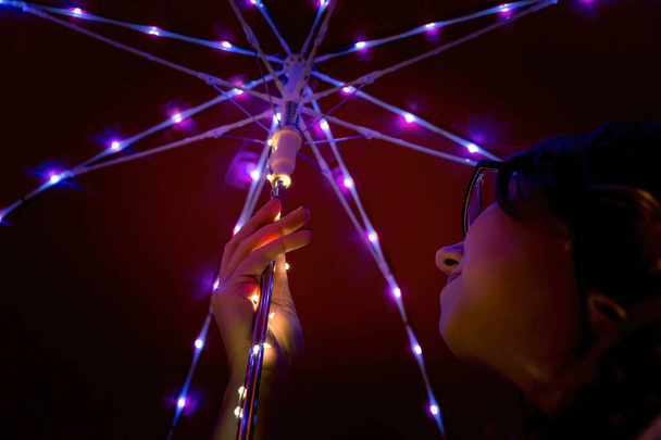A Caucasian female holding a red umbrella with string lights - Foto, afbeelding