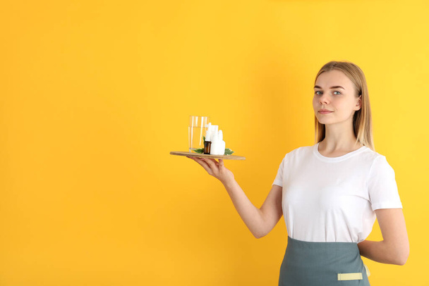 Young woman waiter holds tray with medicines on yellow background - Photo, Image