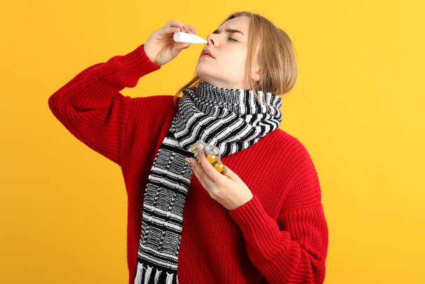 Young woman with nasal drops on yellow background, runny nose concept - Photo, Image