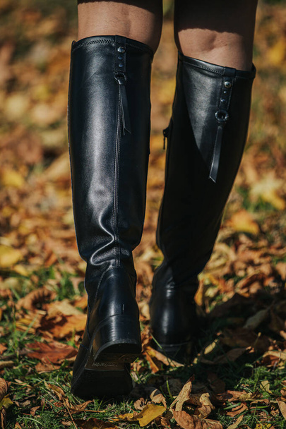 A woman wearing a black fashionable boots while walking on autumnal leaves - Photo, Image