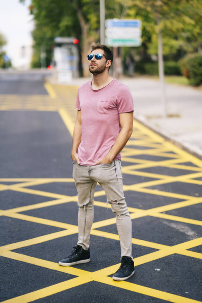 A young Caucasian stylish man wearing a nice pink t-shirt posing on a street - 写真・画像
