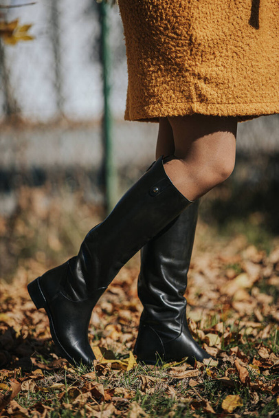 A woman wearing a black fashionable boots while walking on autumnal leaves - Fotó, kép
