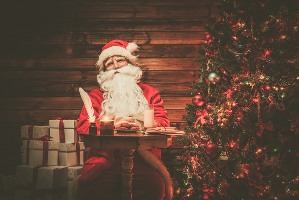 Noel Baba süt ve yulaf ezmesi kurabiye ile masanın arkasında ahşap ev iç oturma - Fotoğraf, Görsel