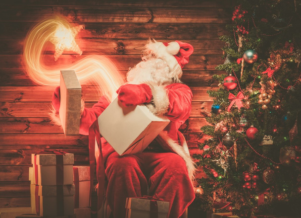 Santa Claus in wooden home interior holding gift box with magic star flying out of it  - Fotografie, Obrázek