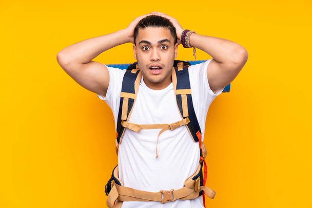 Young mountaineer asian man with a big backpack isolated on yellow background with surprise facial expression - Photo, Image