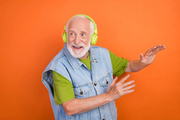 Photo of funny funky retired man wear vintage jeans waistcoat listening music headphones dancing smiling isolated orange color background - Fotó, kép