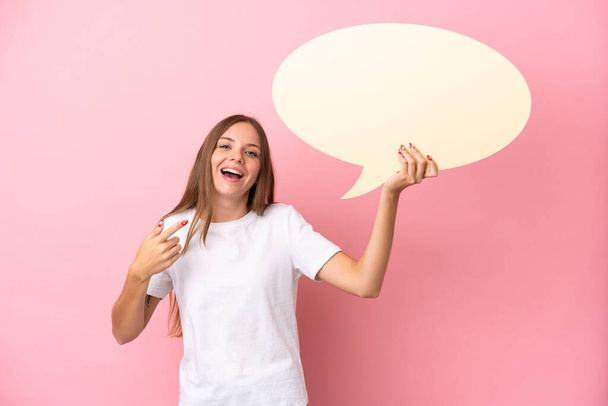 Young Lithuanian woman isolated on pink background holding an empty speech bubble and pointing it - Zdjęcie, obraz