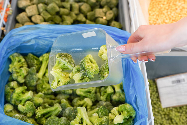 Women hand pick up frozen broccoli in supermarket. - Foto, afbeelding