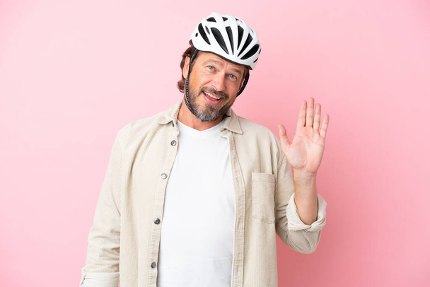 Senior holandský muž s cyklistickou přilbou izolované na růžovém pozadí salutování s rukou s veselým výrazem - Fotografie, Obrázek