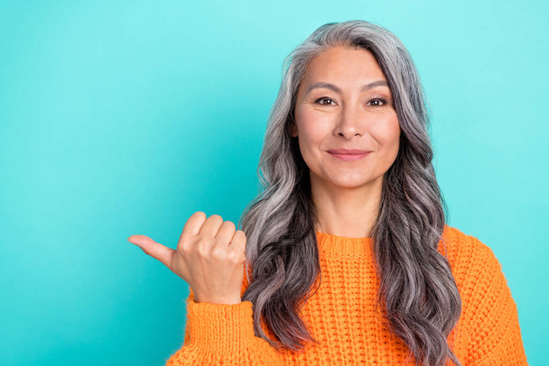 Portrait of attractive cheerful grey-haired woman demonstrating copy space isolated over bright teal turquoise color background. - Photo, image
