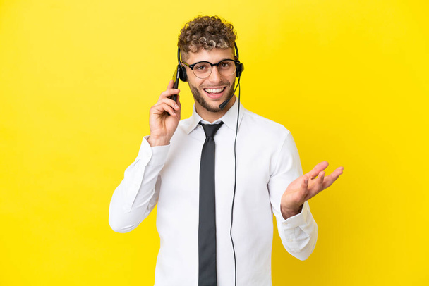 Sarı arka planda izole edilmiş bir kulaklıkla çalışan ve cep telefonuyla konuşan sarışın bir adam. - Fotoğraf, Görsel
