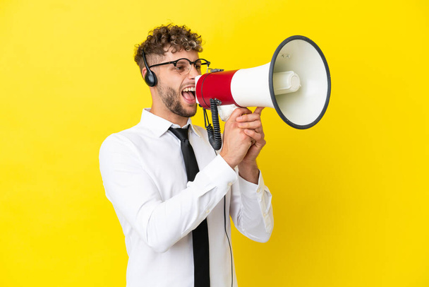 Telemarketer blonde man working with a headset isolated on yellow background shouting through a megaphone - Fotoğraf, Görsel