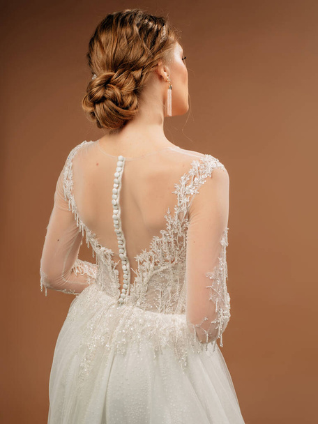 Beautiful wedding dress, rear view. Fashionable bridal gown with tender french lace, long sleeves, white fabric-covered buttons. Beautiful shot in studio on beige background. - Photo, Image