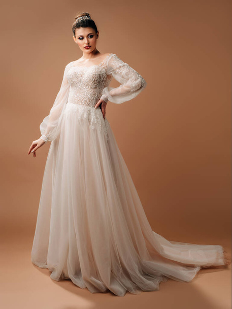 Hochzeitsinspiration. Elegantes kaukasisches Modell in weißem Brautkleid mit Spitze und langen Ärmeln. Ganztägiges Porträt der jungen lächelnden Braut im Studio - Foto, Bild