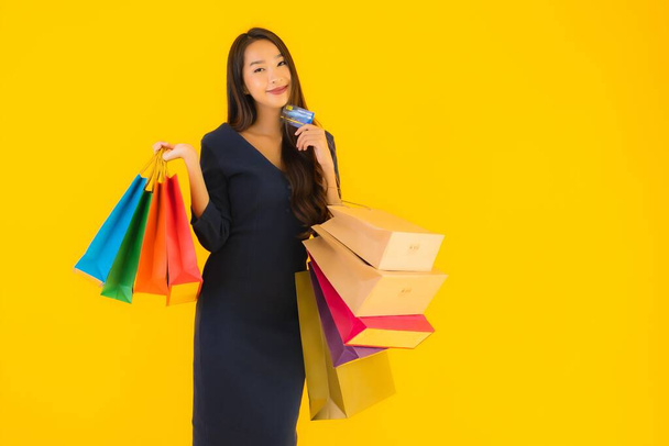 Portrét krásná mladá asijská žena s nákupní taškou kreditní karty a chytrý mobilní telefon žluté izolované pozadí - Fotografie, Obrázek