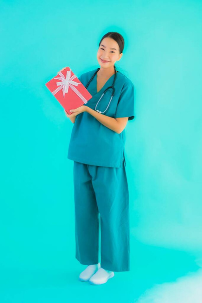 Güzel bir portre genç Asyalı doktor kadın mavi izole arka planda kırmızı hediye kutusu gösteriyor. - Fotoğraf, Görsel