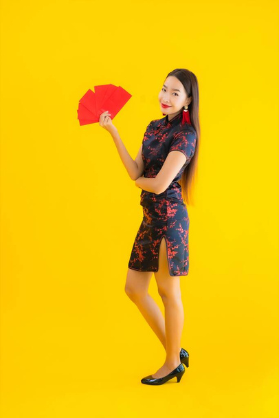 Портрет красивая молодая азиатская женщина носить китайское платье с Ang Pao или красное письмо с наличными за китайский новый год концепции на желтом изолированном фоне
 - Фото, изображение
