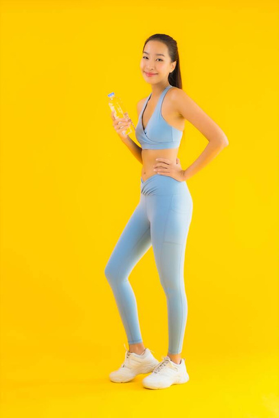 Portrait beautiful young asian woman with bottle water on yellow isolated background - 写真・画像