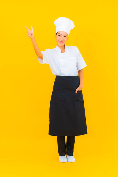 Портрет красивої молодої азіатки в кухарі або кулінарній формі з капелюхом на жовтому ізольованому фоні
 - Фото, зображення