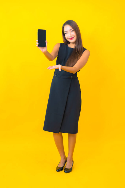 Porträt schöne junge asiatische Geschäftsfrau mit Kaffeetasse und Smartphone auf gelbem Hintergrund - Foto, Bild