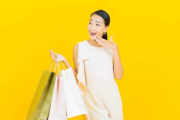Portret mooie jonge aziatische vrouw glimlach met boodschappentas op gele kleur achtergrond - Foto, afbeelding