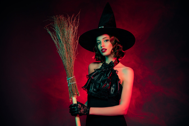 魅惑的な神秘的な女性の写真は、セクシーな魔女のドレスのヘッドウェアのブロムスティック隔離された暗い赤の色の背景を身に着けている - 写真・画像