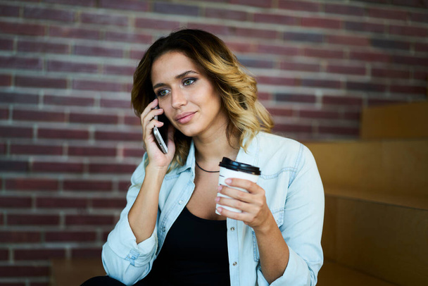 Caucasian hipster girl with takeaway coffee to go connecting to roaming internet for making consultancy cell conversation during service communication, female discussing caffeine taste while phoning - Photo, image