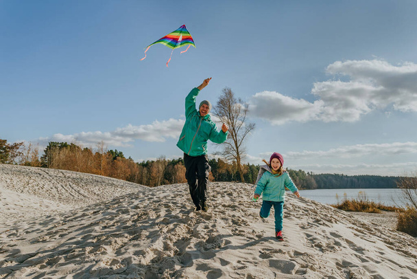 Father with his 5 years old daughter flying a kite on the sand beach. Happy family activities outdoor. Parenthood concept. - 写真・画像
