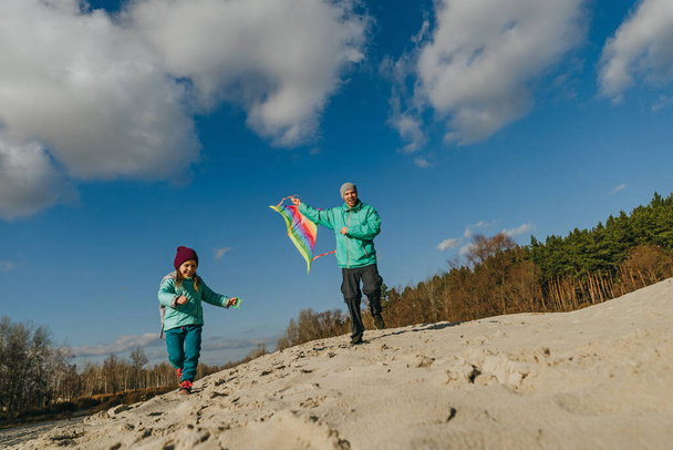 Otec se svou pětiletou dcerou, jak pouští draka na písečnou pláž. Šťastné rodinné aktivity venku. Pojem rodičovství. - Fotografie, Obrázek