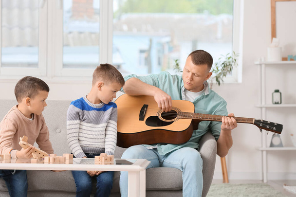 Πατέρας παίζει κιθάρα και μικρά παιδιά περνούν χρόνο μαζί στο σπίτι - Φωτογραφία, εικόνα