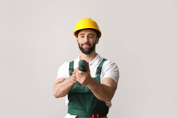 Rakennustyöntekijä kypärässä ruuvipistoolilla kevyellä taustalla - Valokuva, kuva