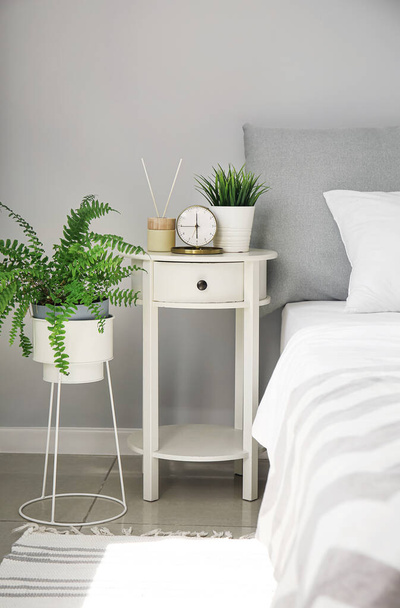 Alarm clock with houseplant and aroma diffuser on white bedside table in bedroom - Photo, image