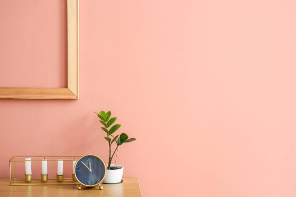 Stylish alarm clock with candles and houseplant on table near pink wall background - Φωτογραφία, εικόνα