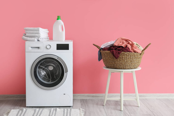 Cesta de vime com lavandaria e máquina de lavar roupa perto da parede rosa - Foto, Imagem
